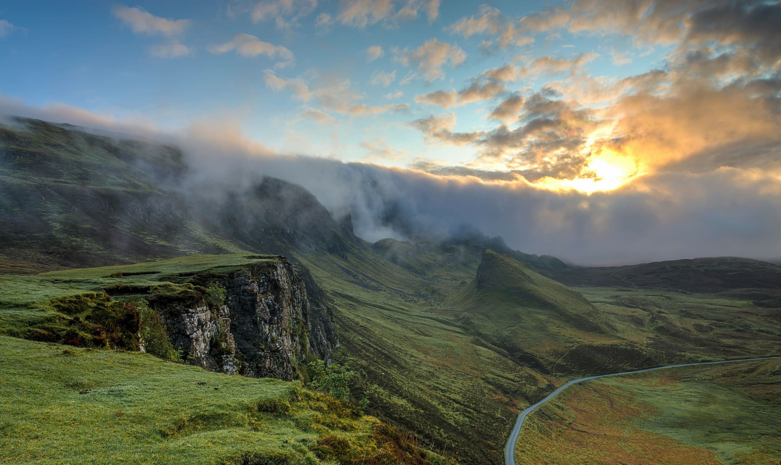 Empty mountain road winding through a misty valley at sunrise
